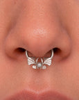 Silver septum piercing ring with a pearl and ornate wing design on a person's nose