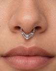 Detailed view of a silver septum ring with a central pearl and small diamonds on a person's nose.