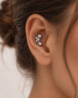 Close-up of a silver leaf-shaped cartilage piercing with a small pearl on a woman's ear.