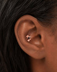 Rose gold flower stud piercing with a black gemstone in a tragus piercing