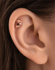 Rose gold flower stud piercing with a black diamond center in a woman's ear helix