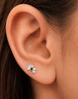 Close-up of a silver ginkgo leaf stud earring with a black gemstone in a human ear.