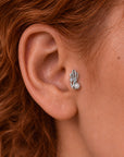 Close-up of a silver floral stud earring with a pearl and diamond on a woman's ear.