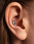 Close-up of a silver flower-shaped tragus piercing with a pearl center in a human ear.
