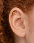Close-up of an 18k gold flower-shaped helix piercing with a small pearl on a human ear.