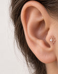 Rose gold flower-shaped ear piercing stud with a small pearl on a person's ear lobe