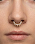 Close-up of a nose with a gold septum piercing adorned with small pearls.