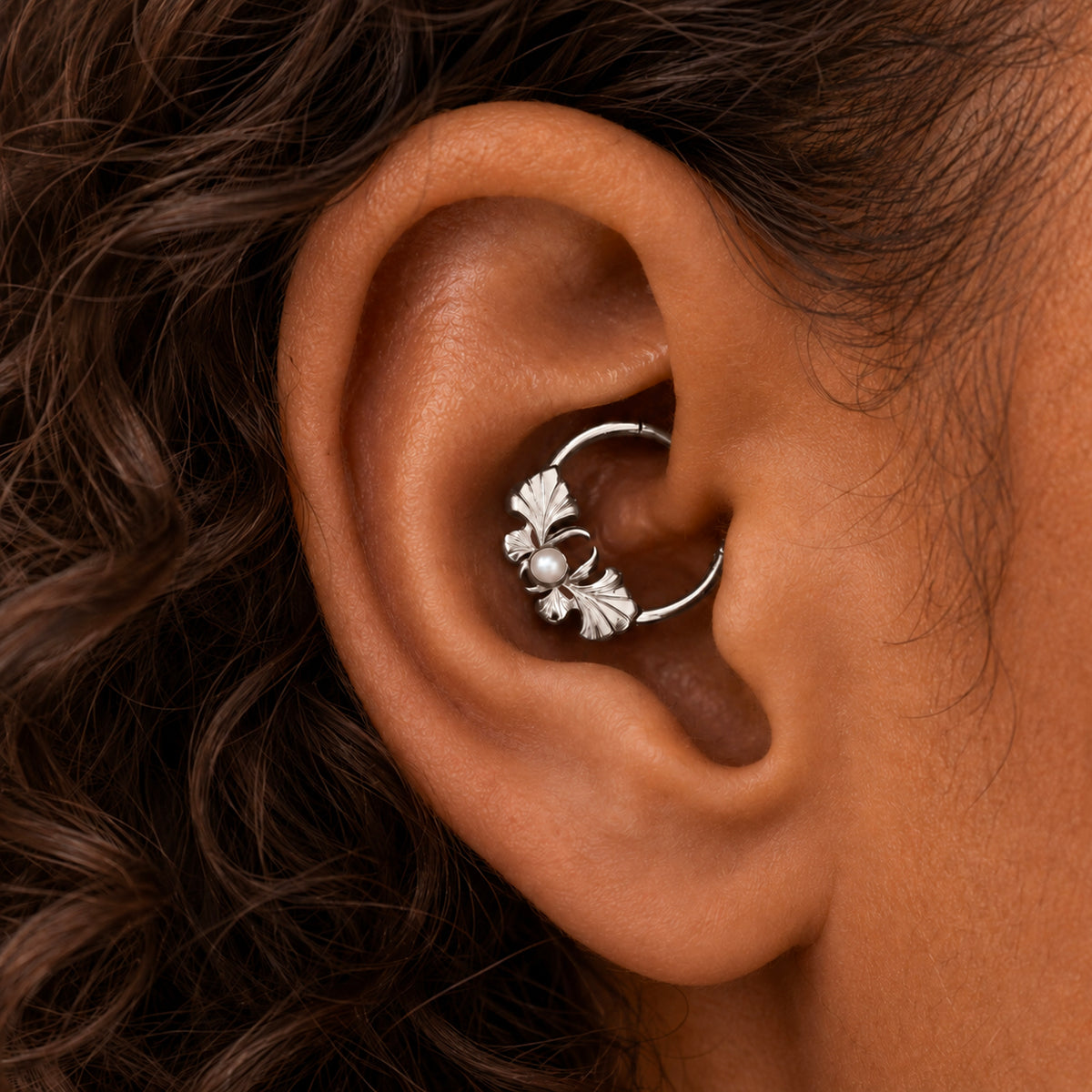 Silver leaf-shaped cartilage piercing hoop with a small pearl detail on a person's ear