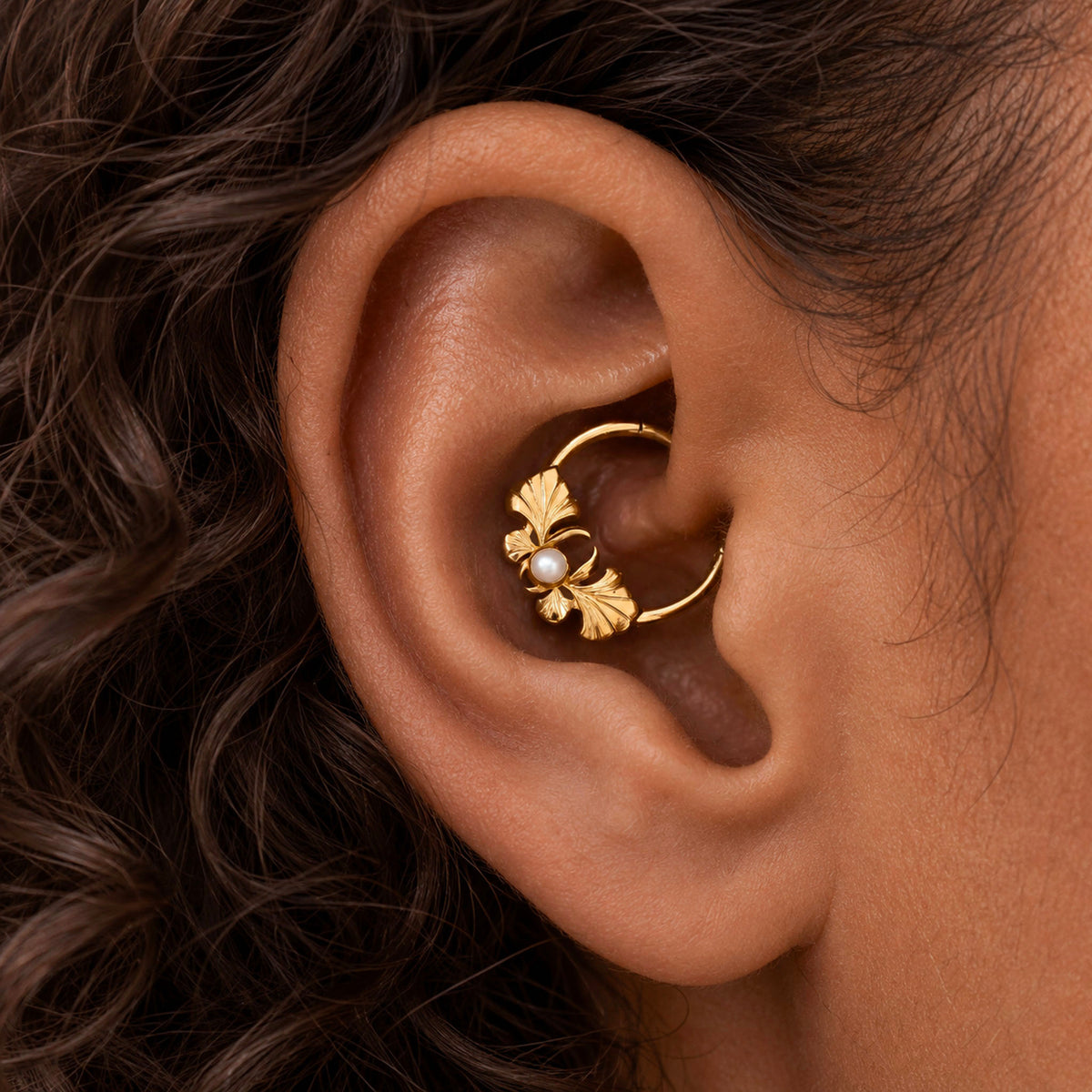 Detailed view of an 18k gold conch piercing hoop featuring a leaf design and a small pearl.