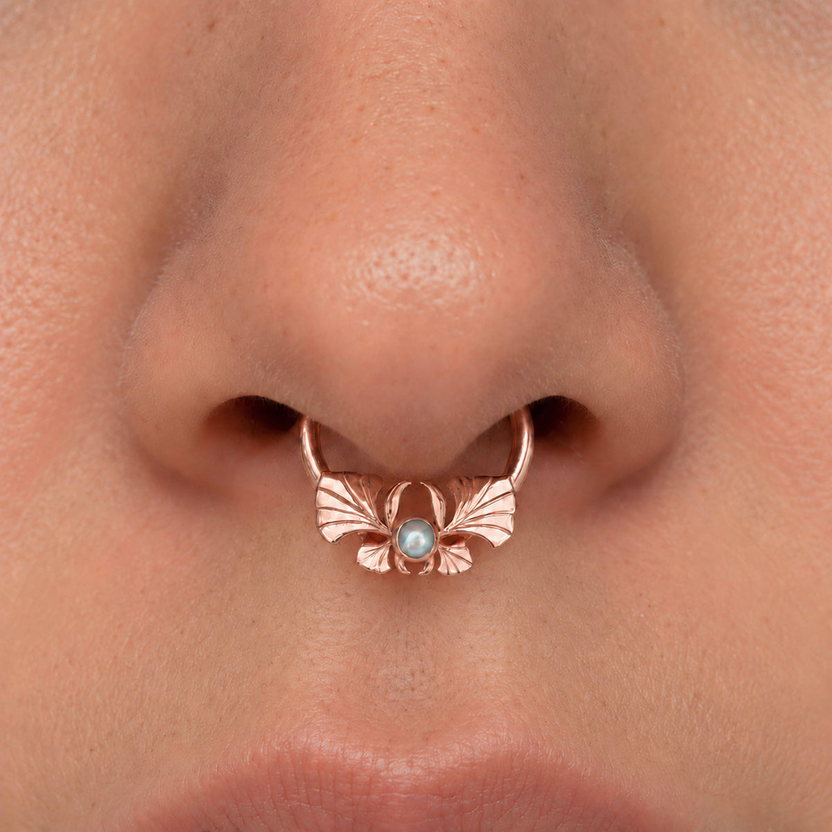 Close-up of a rose gold septum piercing ring featuring a bow design with a central pearl