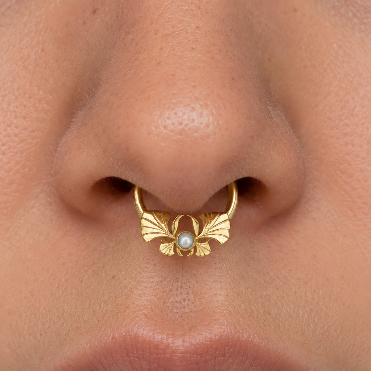 Close-up of a luxury 18k gold septum ring with a pearl and ornate floral design.