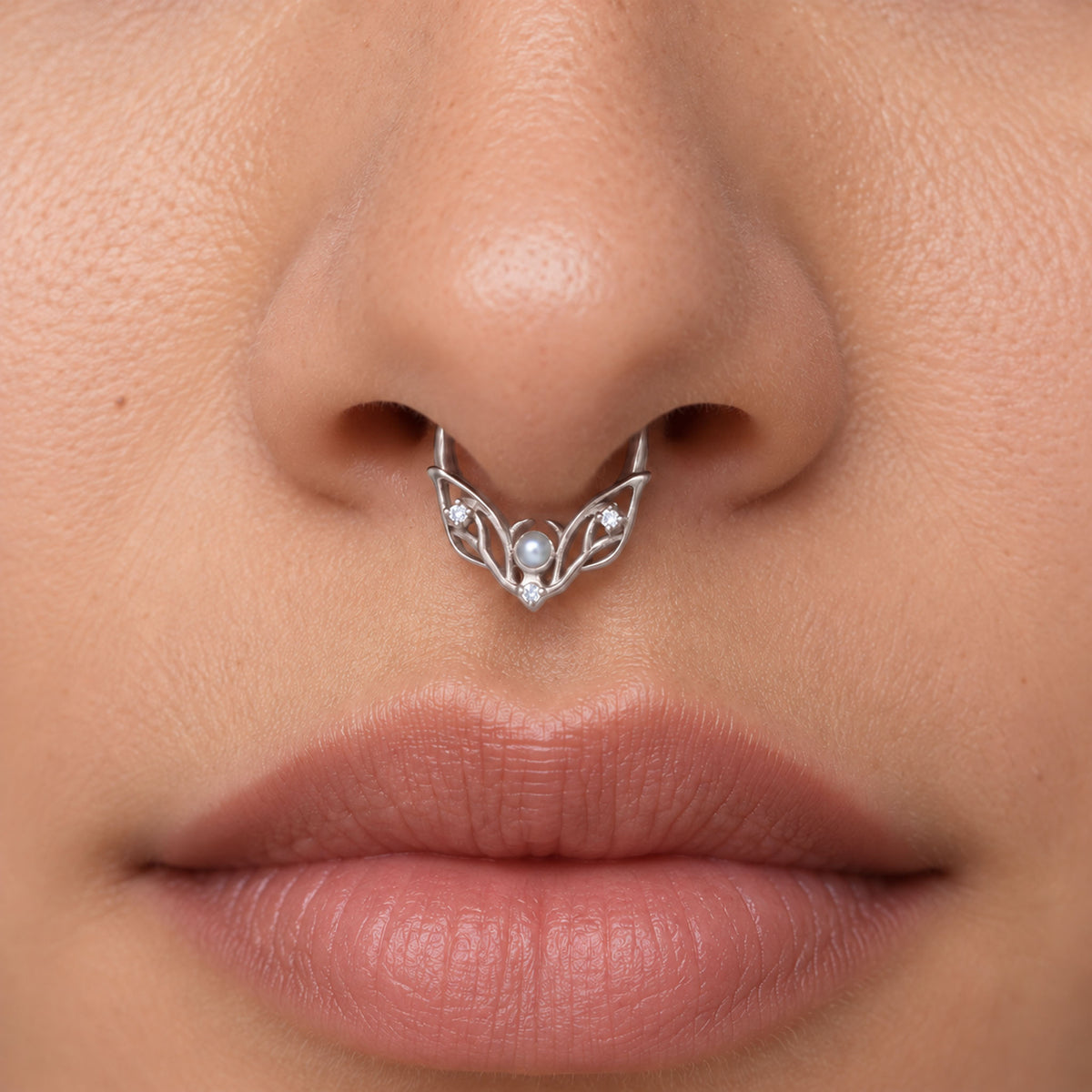 Detailed view of a silver septum ring with a central pearl and small diamonds on a person's nose.
