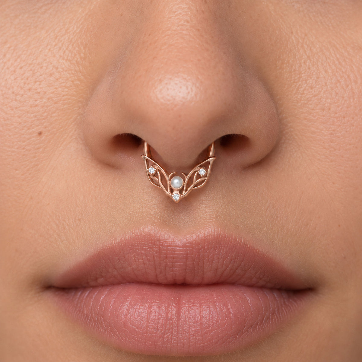 Close-up of a rose gold septum ring with a central pearl and diamonds on a person's nose