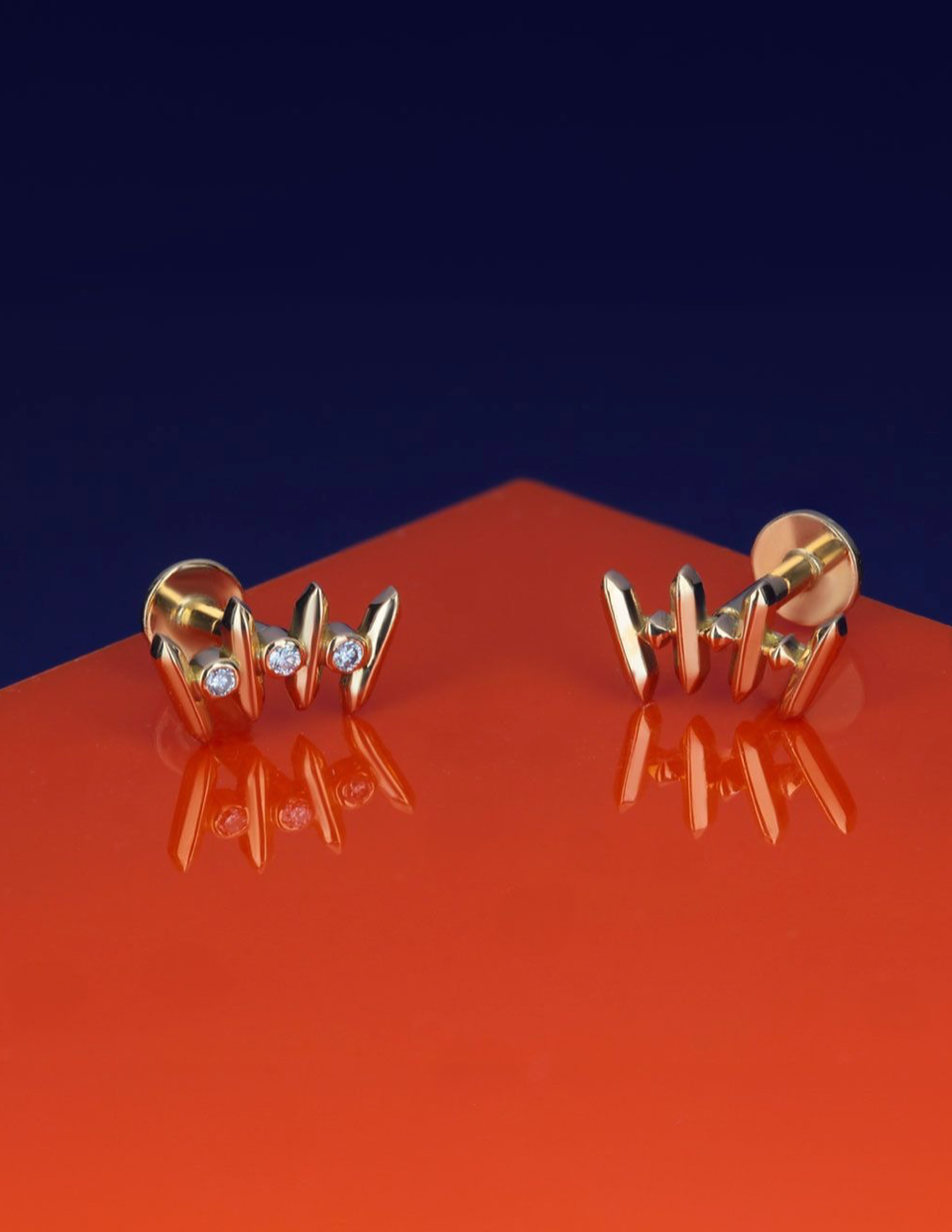 Pair of 18k gold stud earrings with geometric spikes and diamonds on orange surface