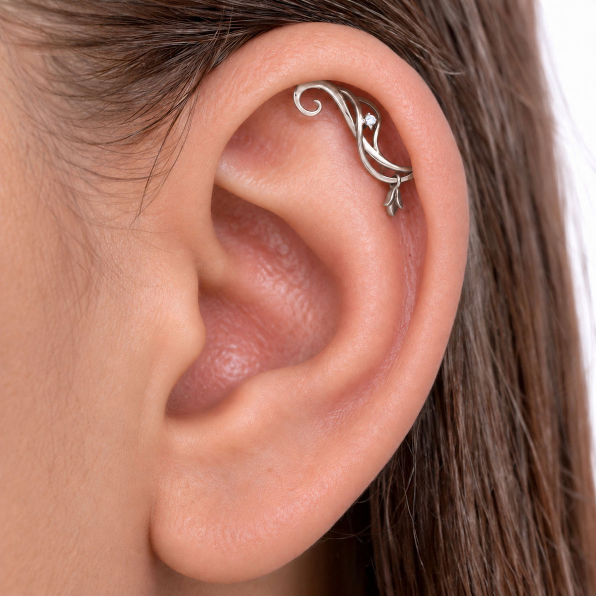 Close-up of a silver filigree helix piercing with a small diamond in a human ear.
