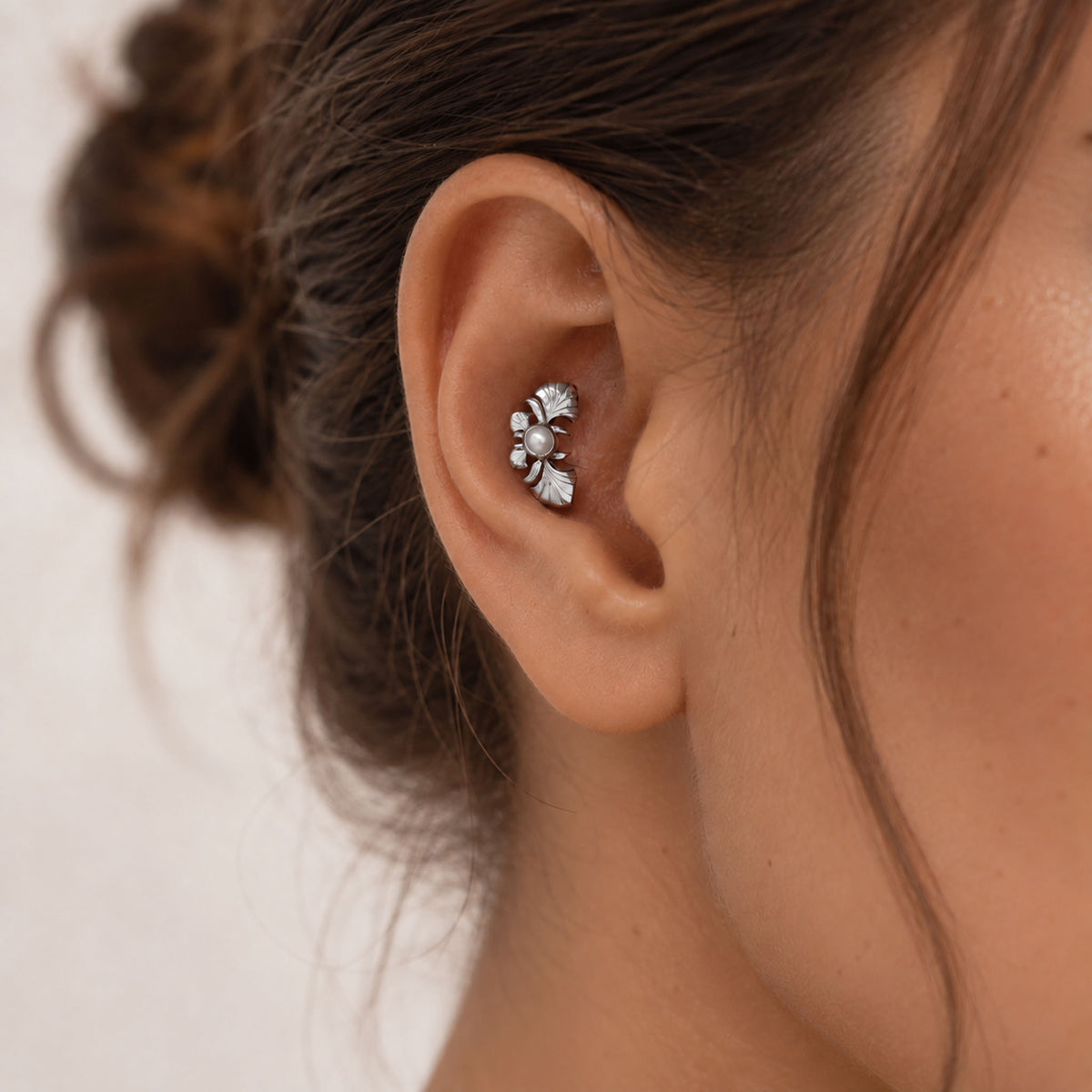 Close-up of a silver leaf-shaped cartilage piercing with a small pearl on a woman's ear.