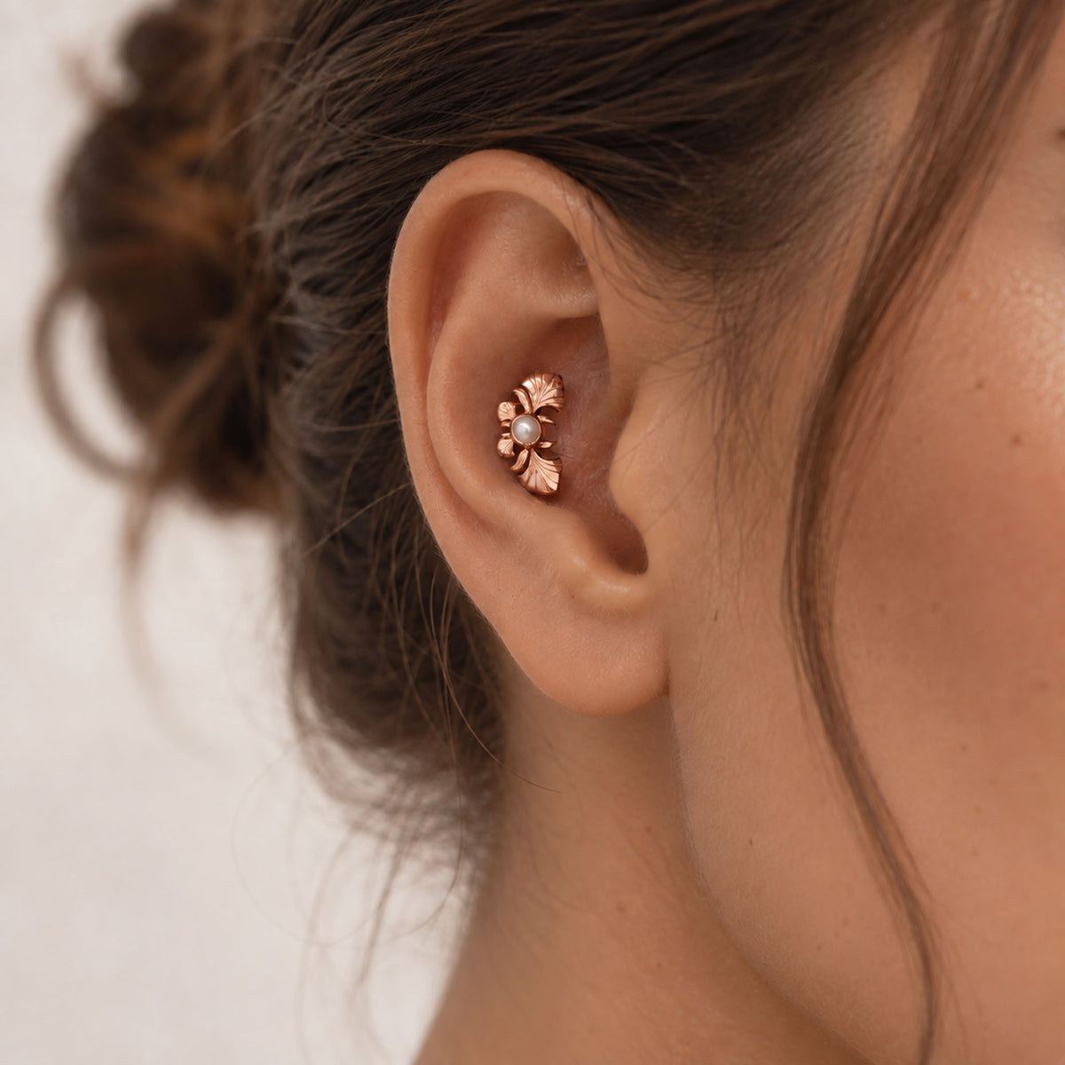 Close-up of a rose gold leaf and pearl helix piercing in a woman's ear.