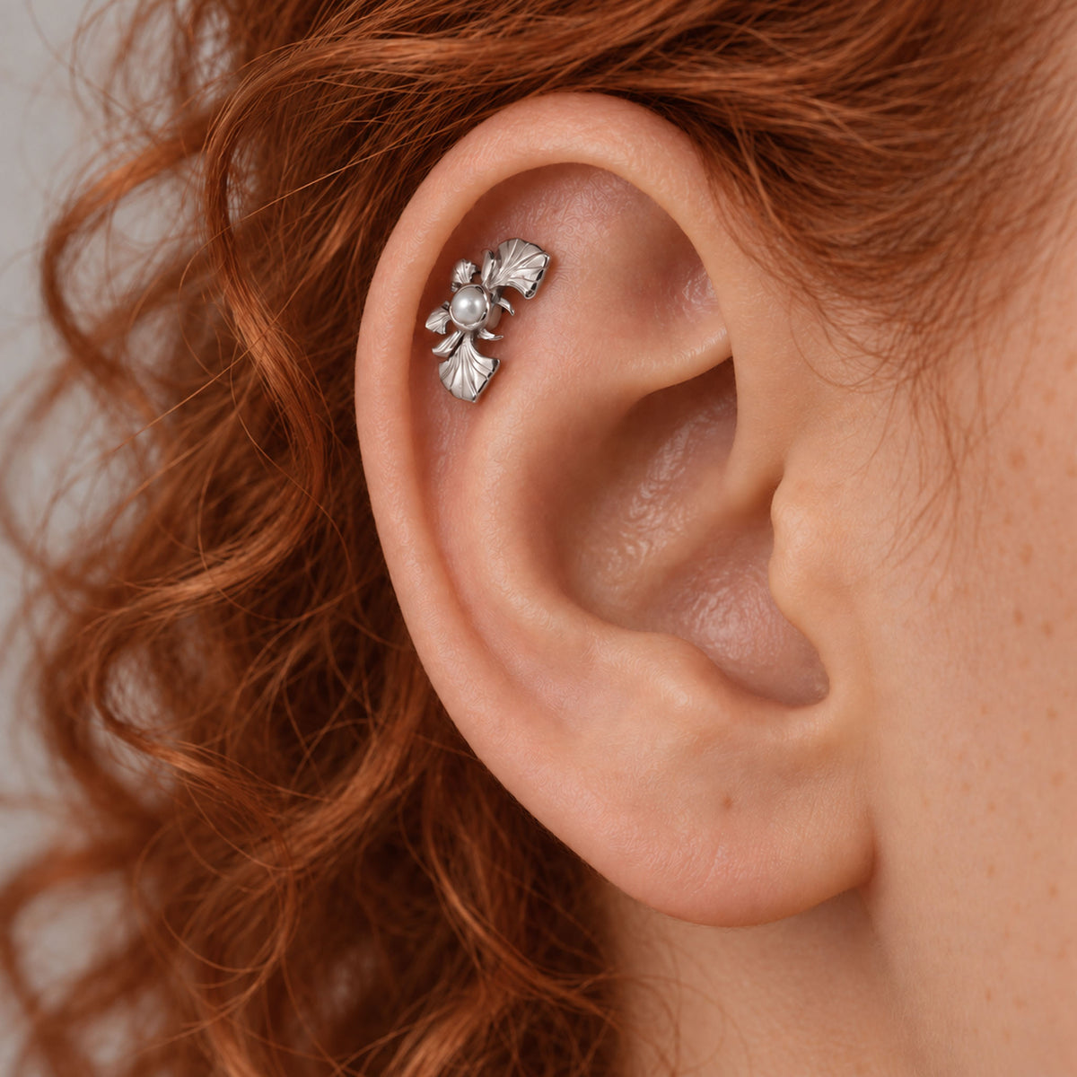 Close-up of a silver leaf and pearl helix piercing in a person's ear.