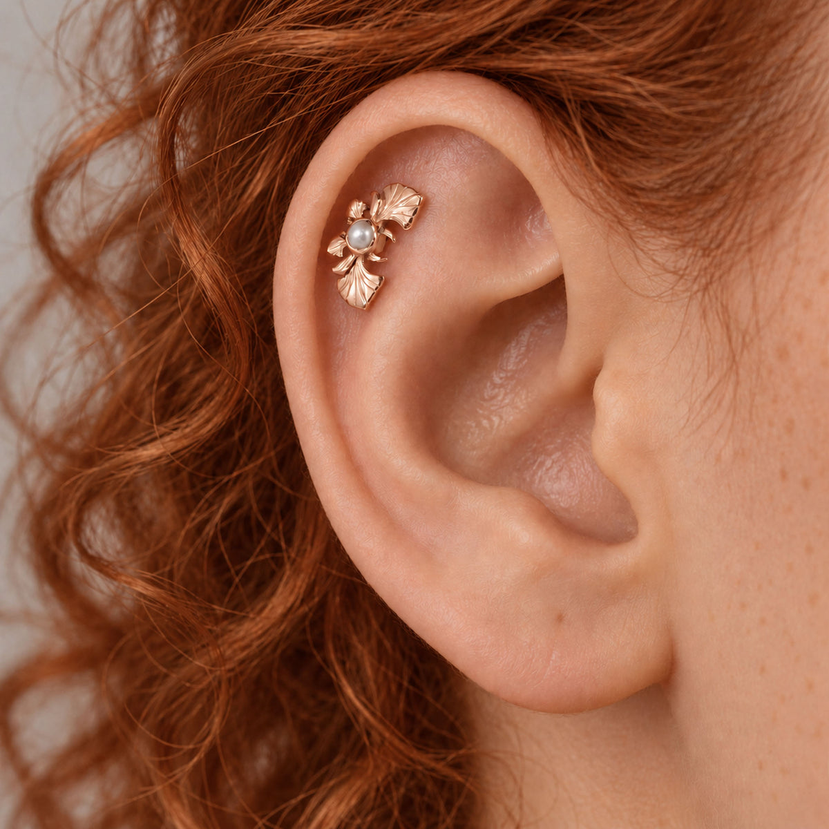 18k gold leaf helix piercing with a small pearl on a person's ear
