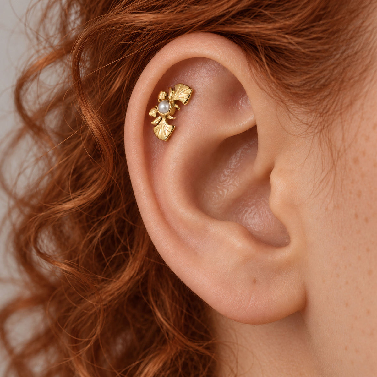Close-up of a gold leaf cartilage piercing with a small pearl in a human ear