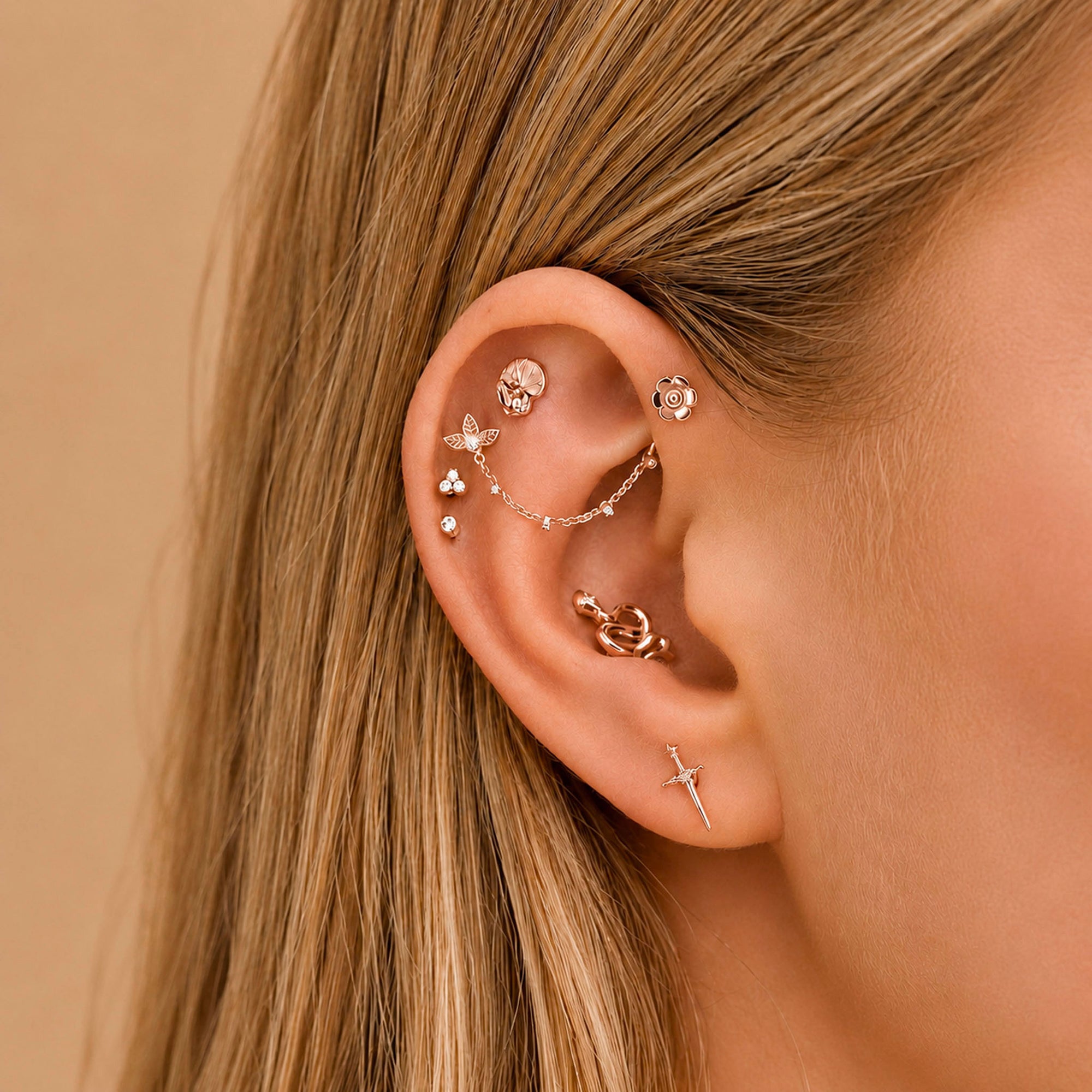 Elegant 18k gold ear piercings with floral, butterfly & sword designs, adorned with diamonds for a luxury look.