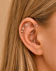 Elegant 18k gold ear piercings with floral, butterfly & sword designs, adorned with diamonds for a luxury look.