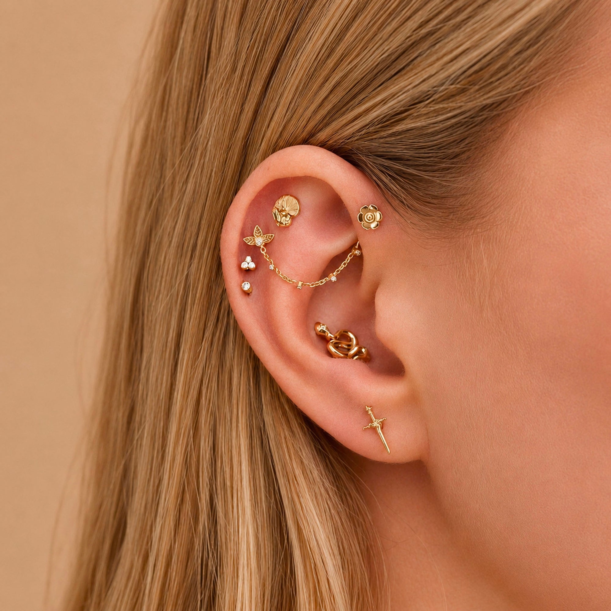 18k gold ear piercings with floral, chain, and sword designs, adorned with tiny crystals for elegant body jewelry.