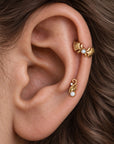 Close-up of a human ear with 18k gold pearl helix and lobe piercing jewelry.
