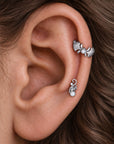 Two silver ear piercings featuring pearls and ornate floral designs on a human ear.