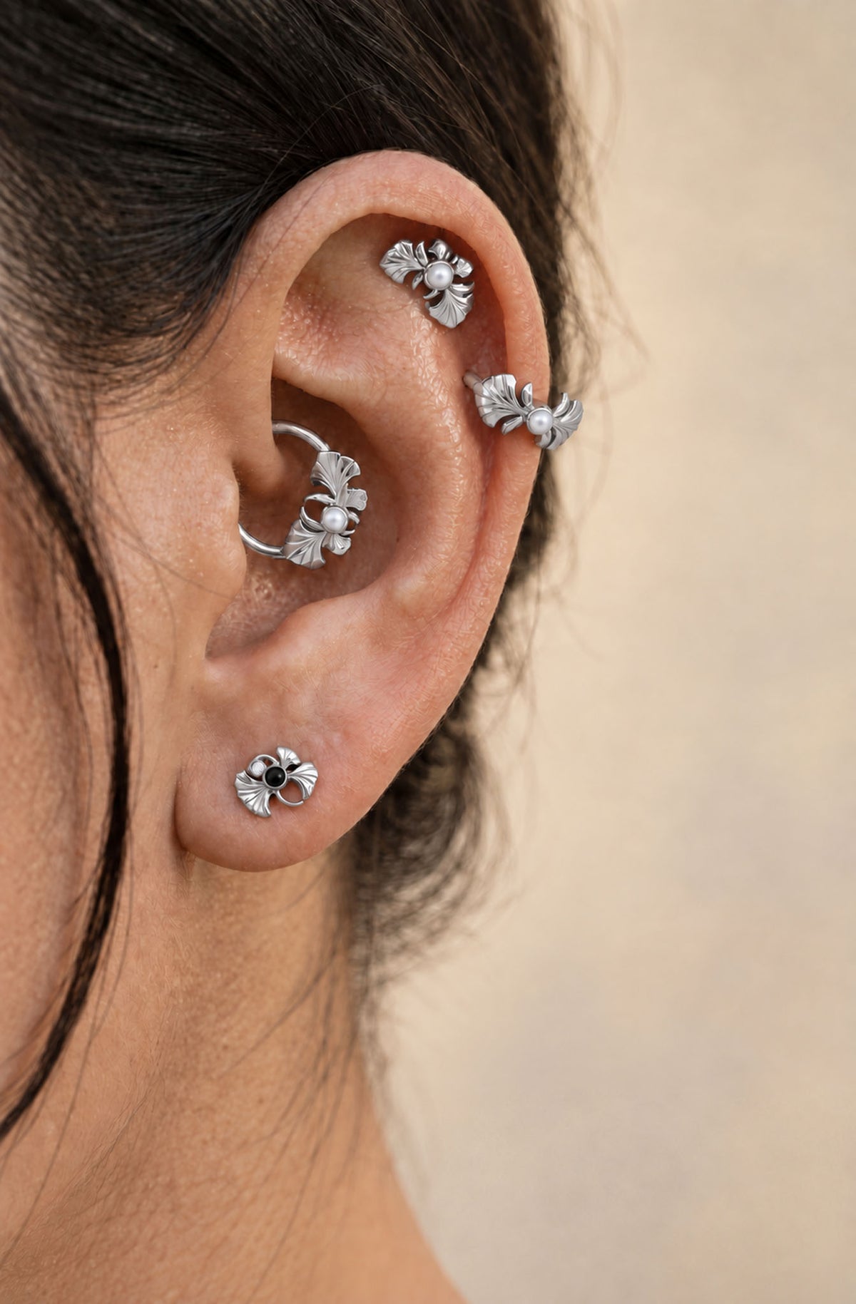 Close-up of a person's ear with silver ginkgo leaf earrings and piercing jewelry.
