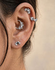 Close-up of a person's ear with silver ginkgo leaf earrings and piercing jewelry.