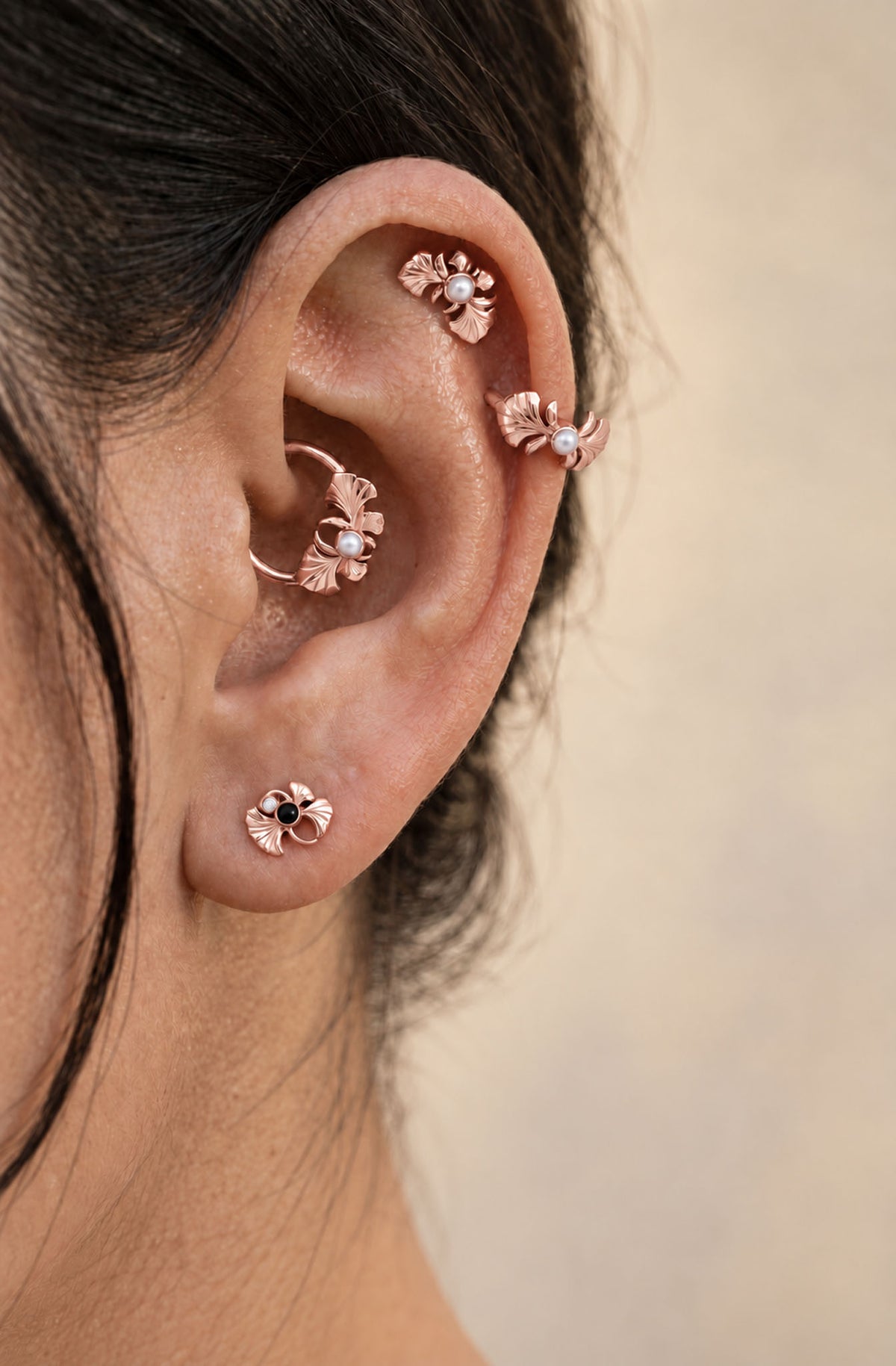 Rose gold leaf-shaped piercing jewelry with pearls and gemstones in a human ear