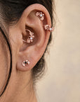 Rose gold leaf-shaped piercing jewelry with pearls and gemstones in a human ear