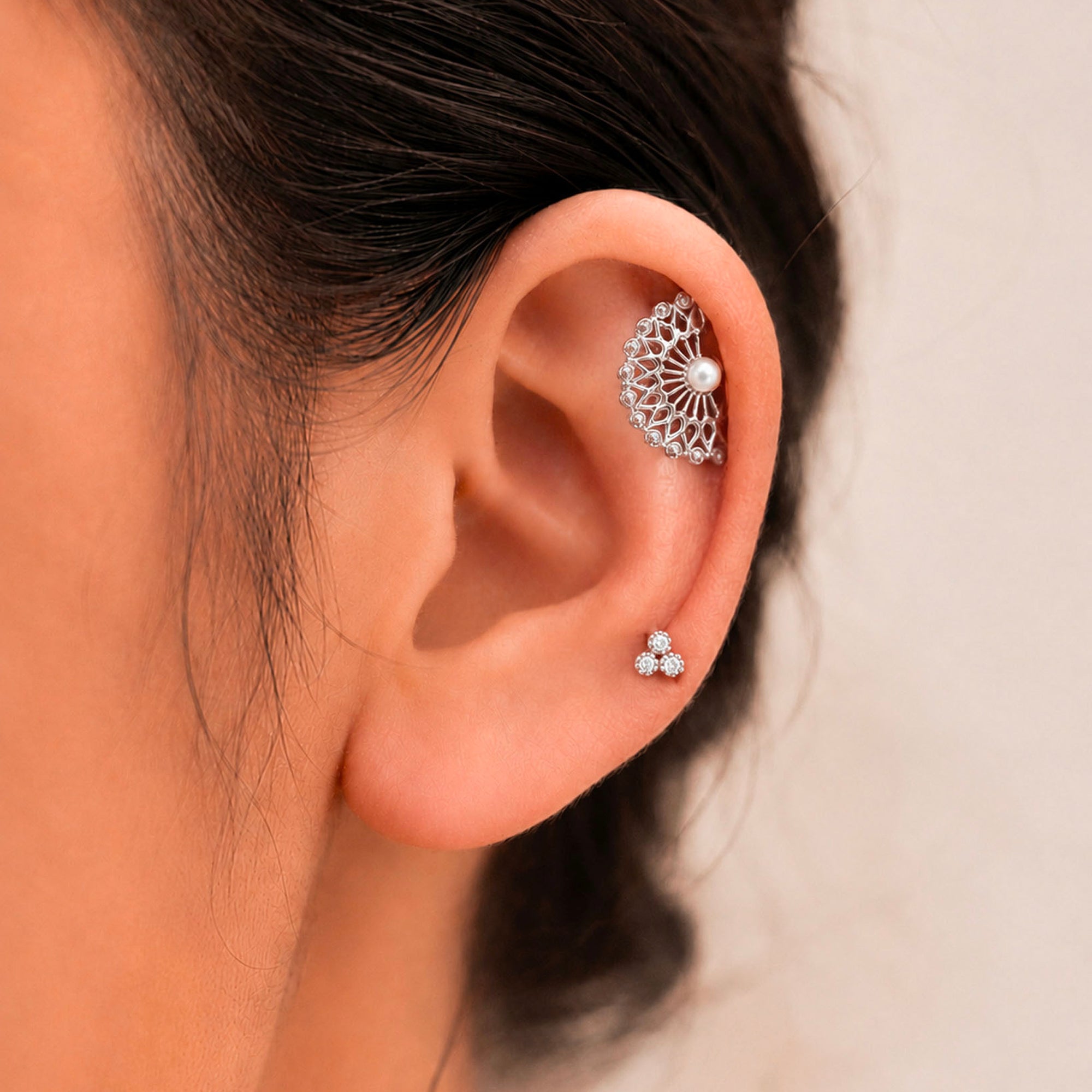 Elegant 18k gold ear cuff with pearl and diamond accents, paired with floral stud earrings for a luxurious look.