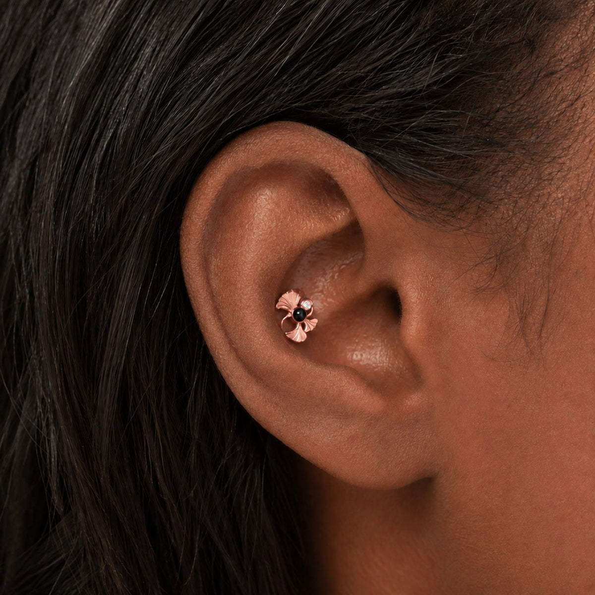Rose gold flower stud piercing with a black gemstone in a tragus piercing
