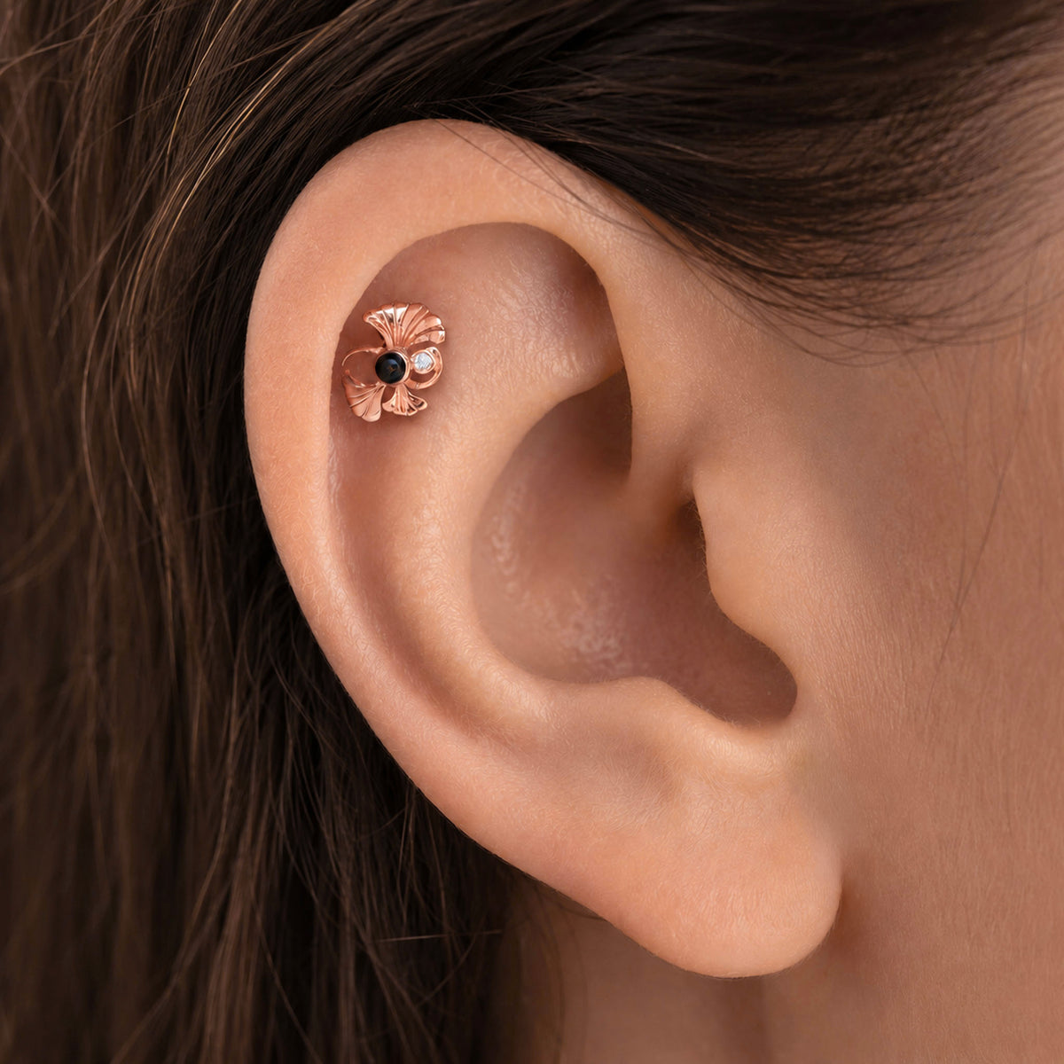 Rose gold flower stud piercing with a black diamond center in a woman's ear helix