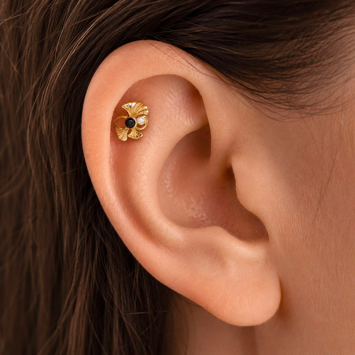 Close-up of a gold flower helix piercing with black and white stones in a woman's ear.