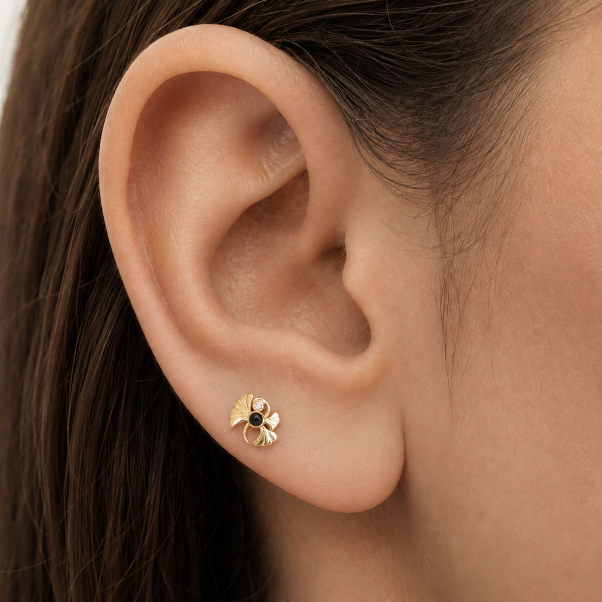 Close-up of a gold flower stud earring with a black center stone in a person's ear lobe.