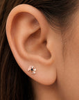 Close-up of a rose gold flower-shaped stud earring with a black stone in a woman's earlobe.