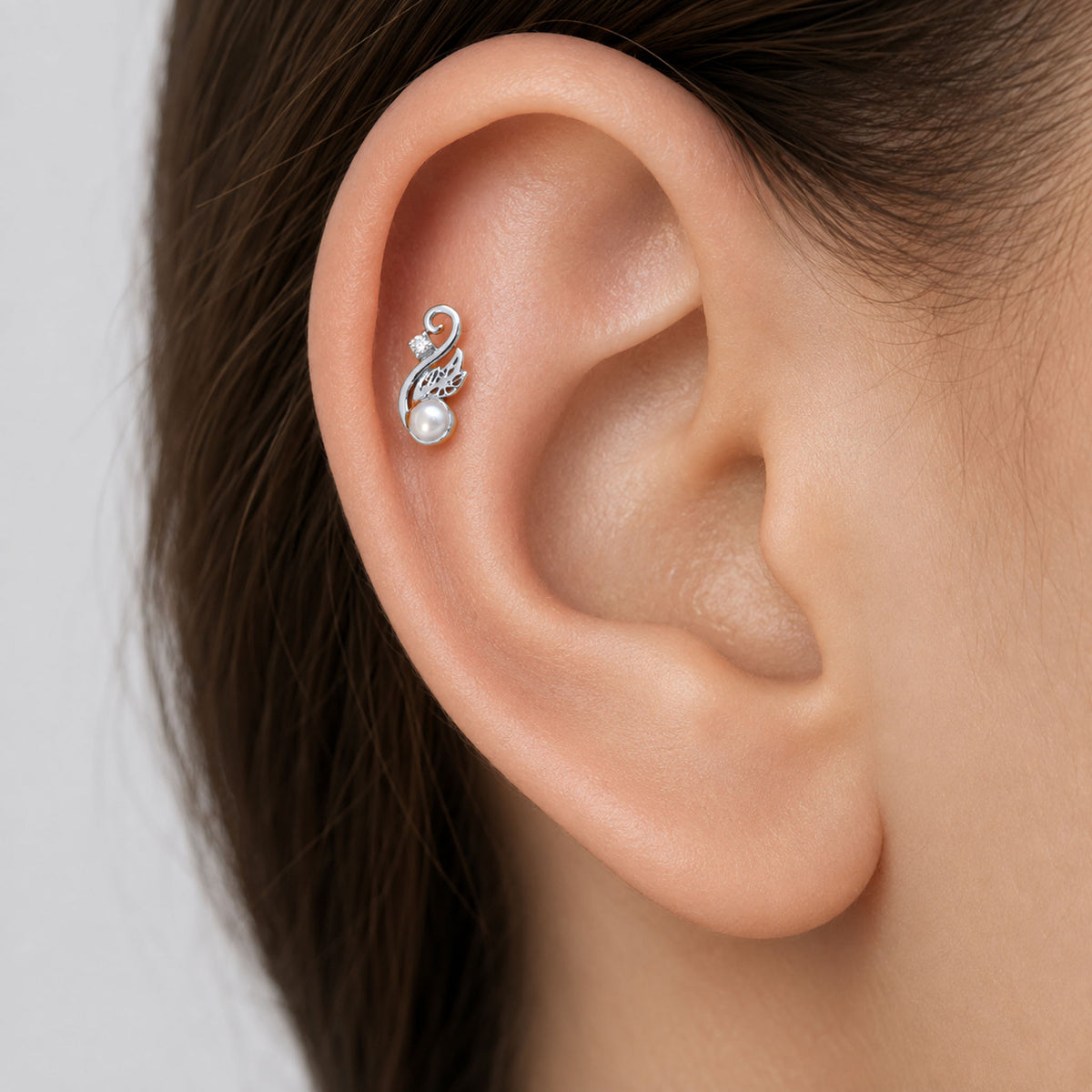 Elegant white gold cartilage piercing with a pearl and diamond swirl design on a human ear