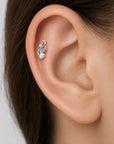 Elegant white gold cartilage piercing with a pearl and diamond swirl design on a human ear
