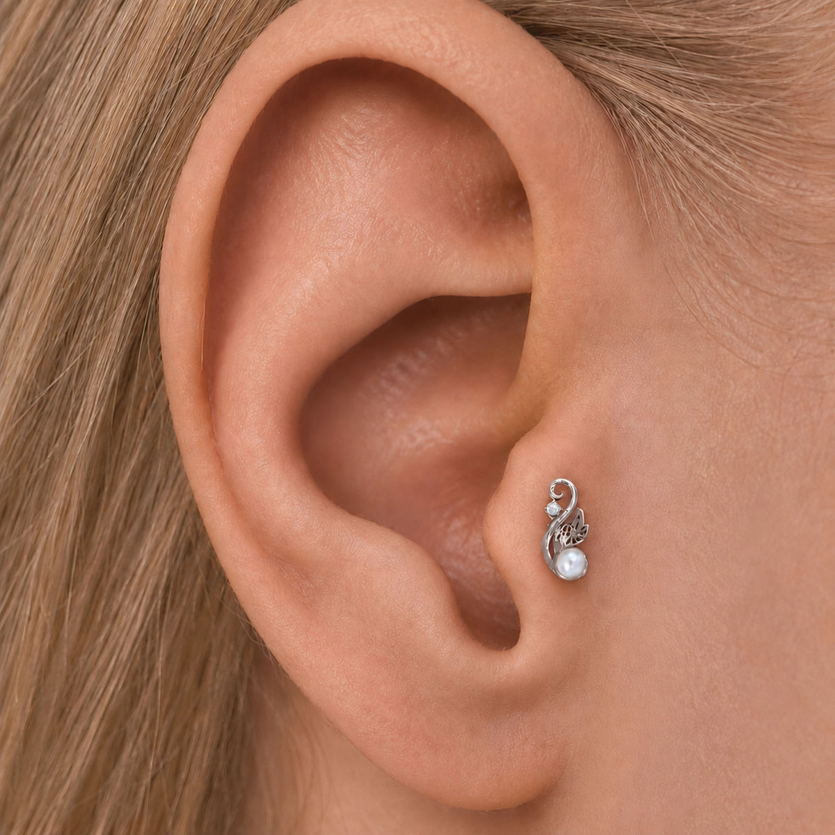 Close-up of a silver floral ear piercing with a small pearl in a woman's earlobe.