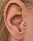 Close-up of a silver floral ear piercing with a small pearl in a woman's earlobe.