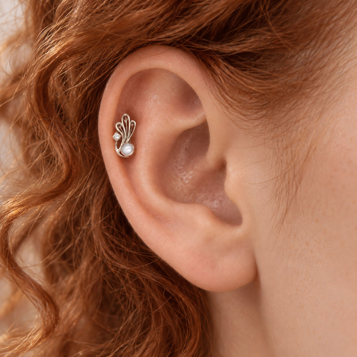 Elegant silver helix piercing with a pearl and small diamond in a leaf design on a human ear
