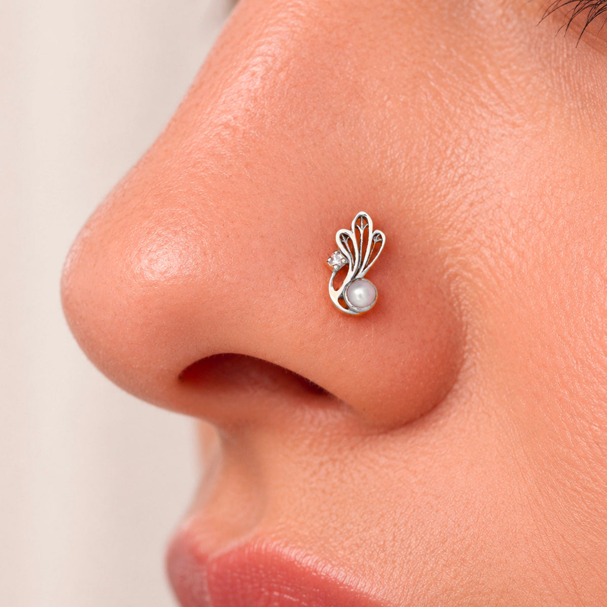Close-up of a silver nose stud with a pearl and diamond accent on a woman's nostril.