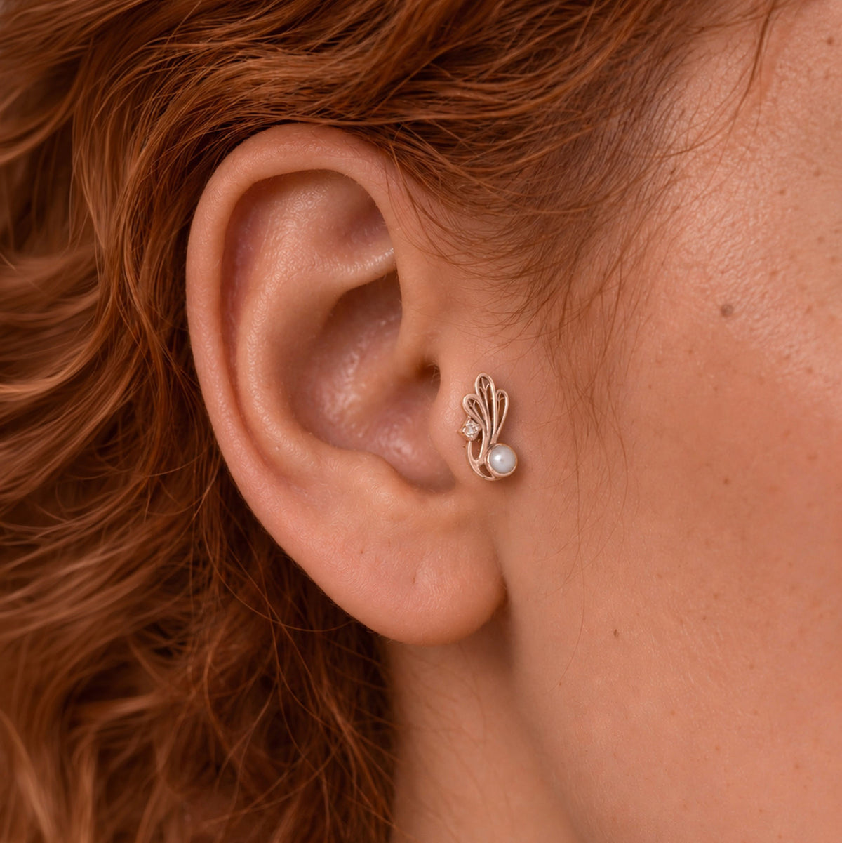 Close-up of a gold leaf and pearl stud earring in a woman's ear lobe