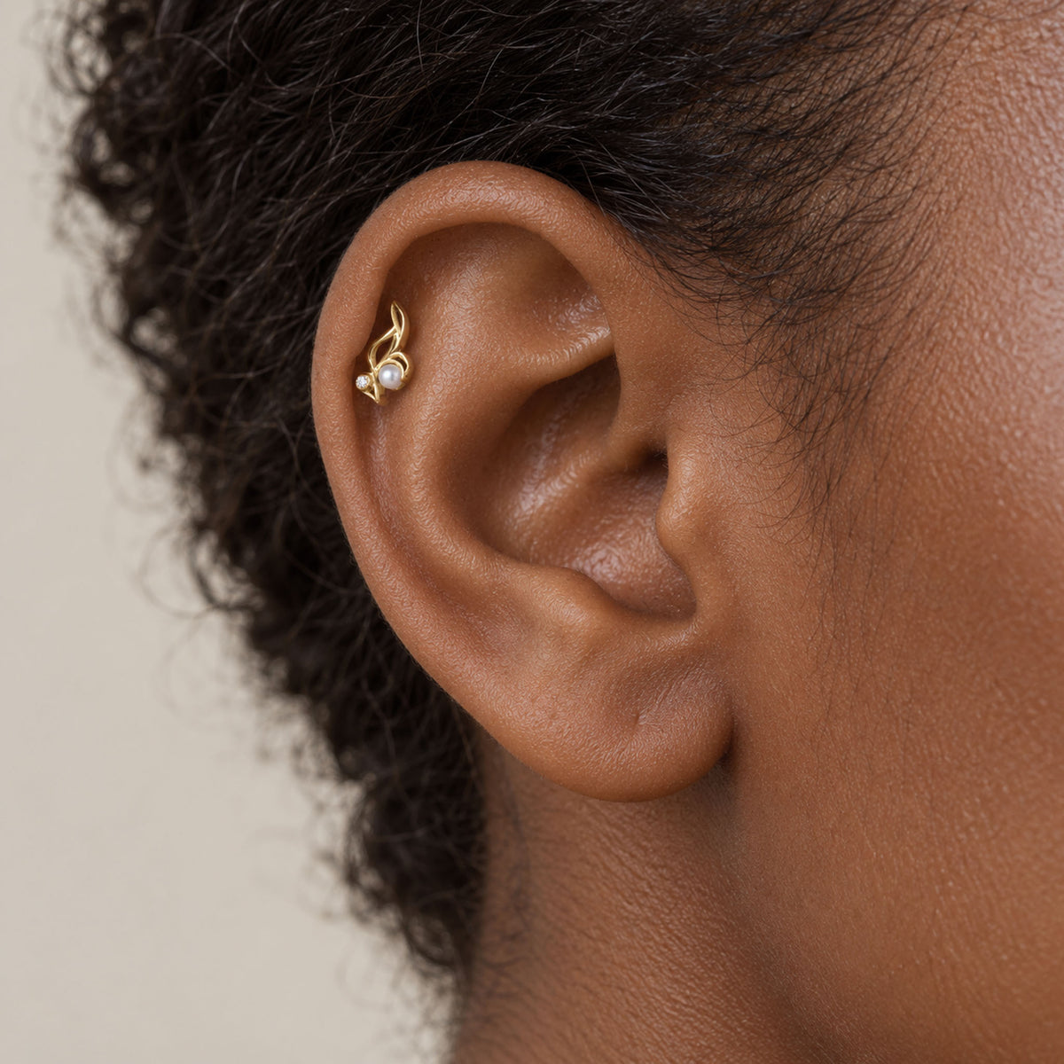 Close-up of a 18k gold helix piercing with a small pearl on a person's ear