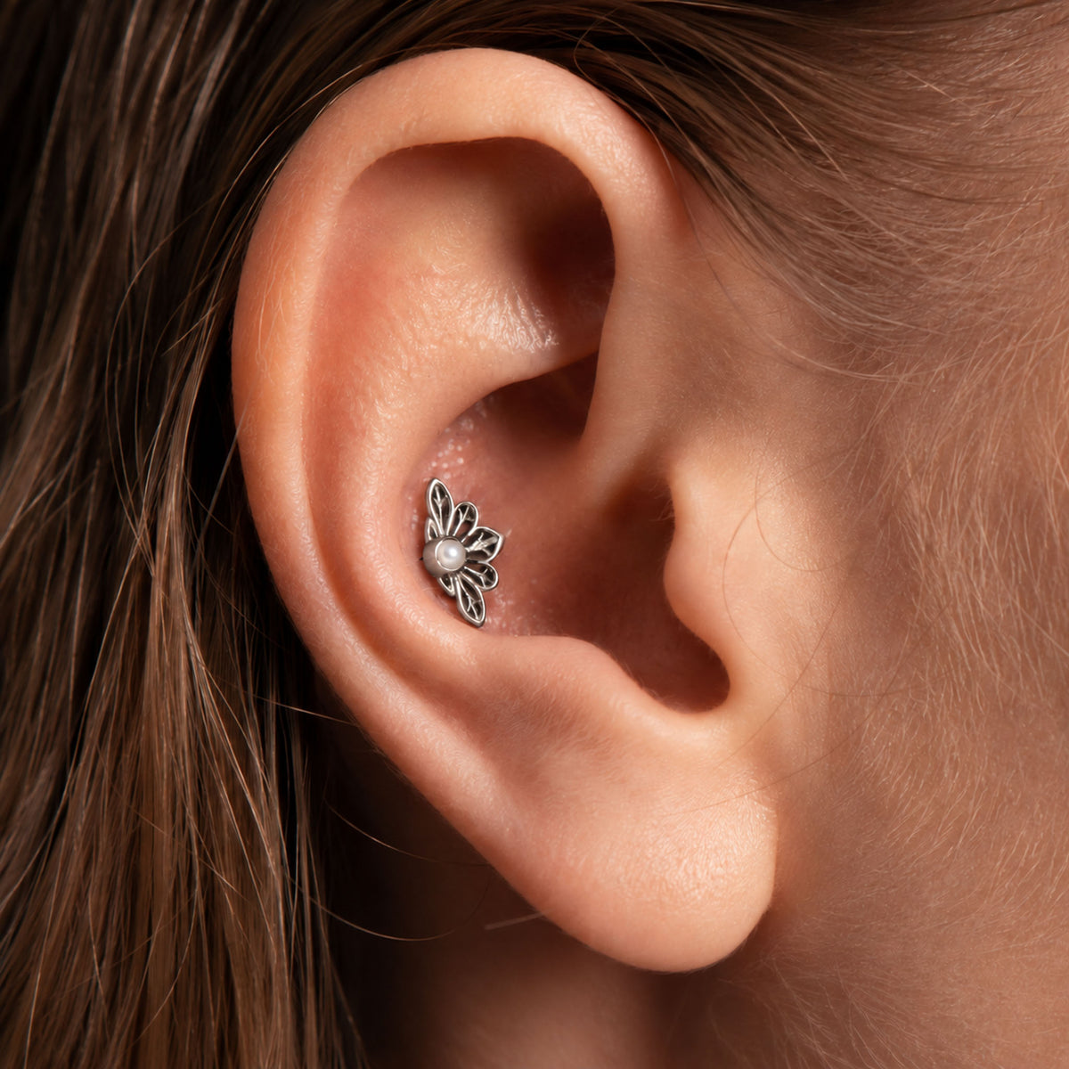 Close-up of a silver flower-shaped tragus piercing with a pearl center in a human ear.