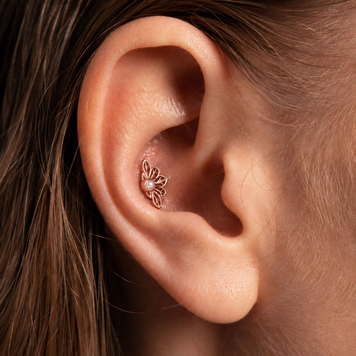 Rose gold flower-shaped stud earring with a pearl center in a tragus piercing