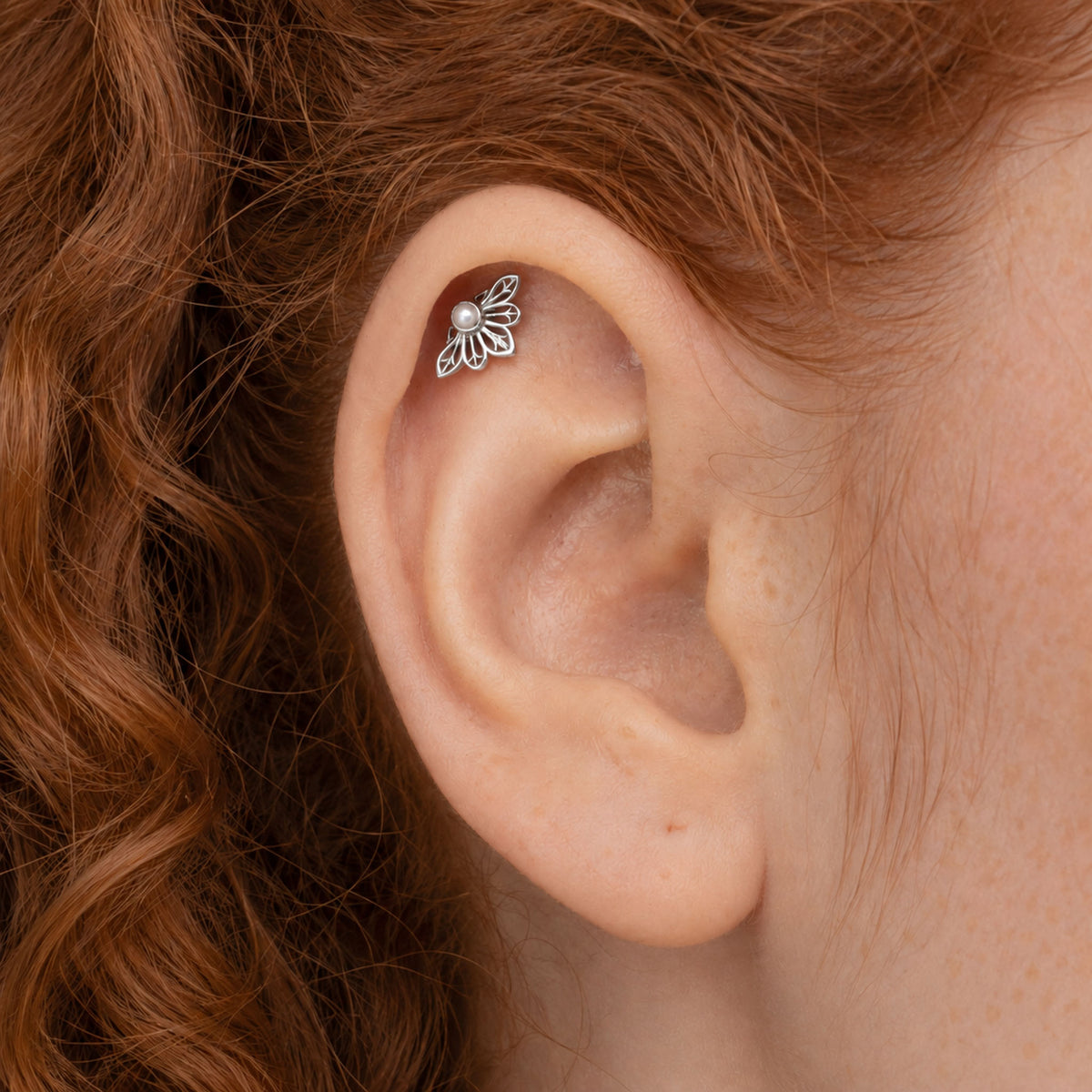 Close-up of a silver floral helix piercing with a small pearl on a woman's ear.